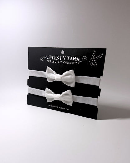 White Velvet Bow Leg Garters with large bow and adjustable elastic straps displayed on a black retail card