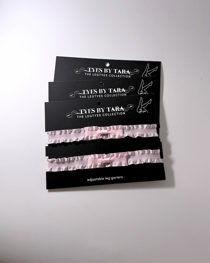 Three black retail cards holding three pairs of light pink ruffled leg garters, branded 'Lys By Tara The Legties Collection', shown against a plain off-white background.