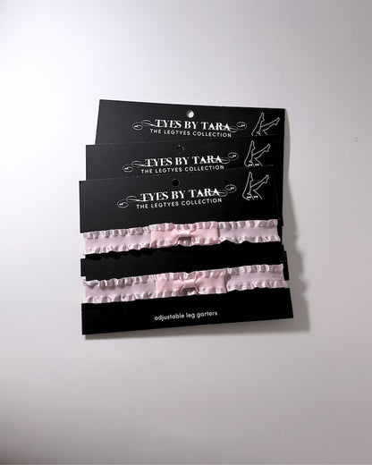 Three black retail cards holding three pairs of light pink ruffled leg garters, branded 'Lys By Tara The Legties Collection', shown against a plain off-white background.