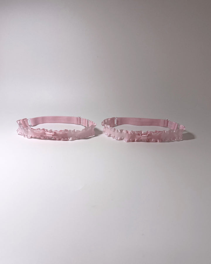 Two light pink ruffled leg garters displayed side-by-side on a plain light gray background.