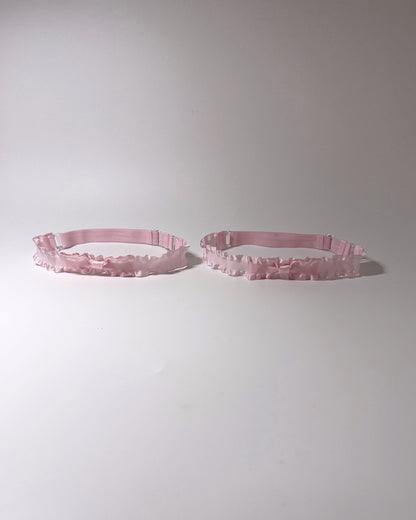 Two light pink ruffled leg garters displayed side-by-side on a plain light gray background.