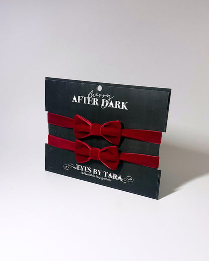 Red velvet leg garters on a softly lit surface on a black card