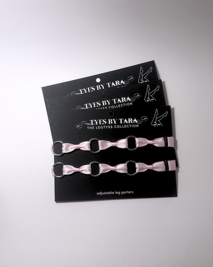 Three pink adjustable leg garters with silver metal rings, displayed on a black branded card that reads 'TYES BY TARA THE LEGTYES COLLECTION'.