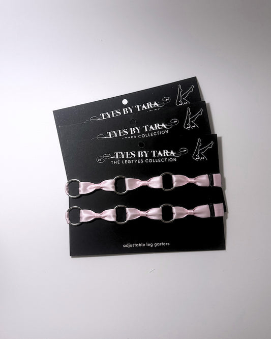 Three pink adjustable leg garters with silver metal rings, displayed on a black branded card that reads 'TYES BY TARA THE LEGTYES COLLECTION'.