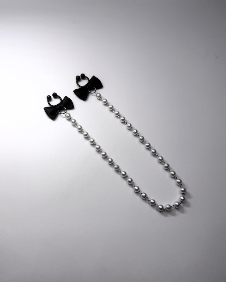 Centerfold Pearl Nipple Clamps with black bows and a creamy pearl strand connecting them side view