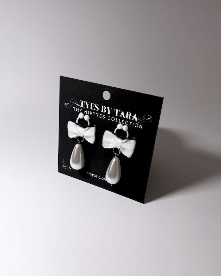 A pair of white bow nipple clamps and teardrop pearls on a black display card labeled 'YYES BY TARA THE NIPTYES COLLECTION'.