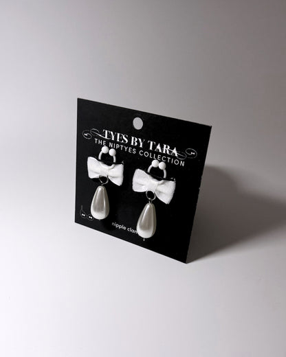 A pair of white bow nipple clamps and teardrop pearls on a black display card labeled 'YYES BY TARA THE NIPTYES COLLECTION'.