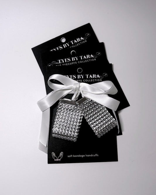Three silver rhinestone-covered soft bondage hand cuffs tied with a white satin ribbon, presented on black retail card 