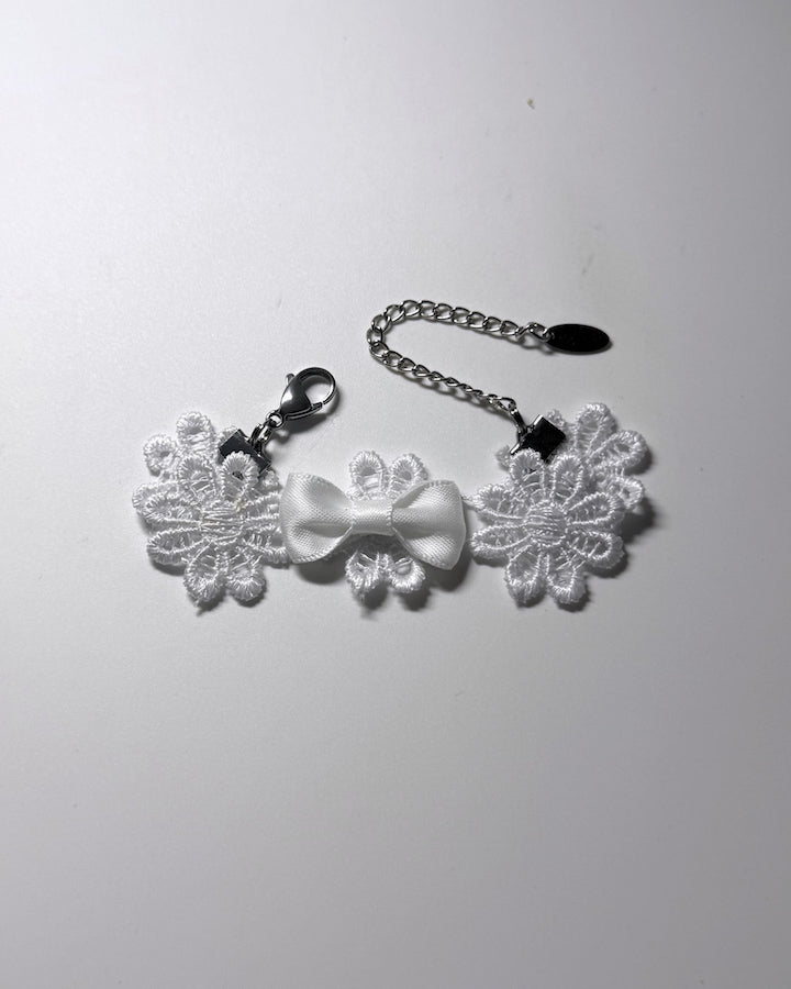 White flower bracelet a central white satin bow, attached to a silver chain with a stainless steel lobster clasp, shown on a plain light gray background