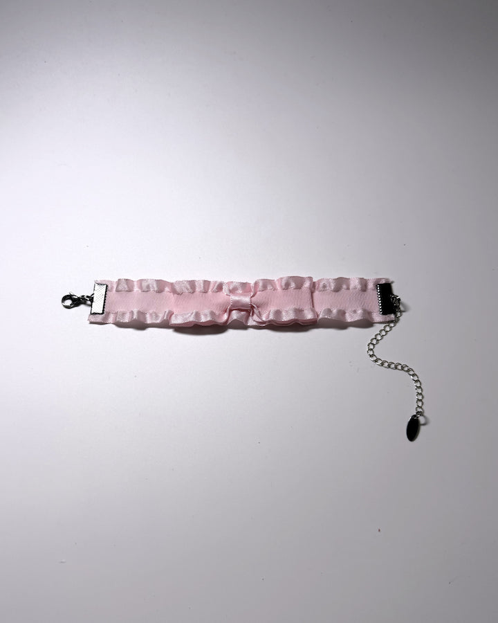 A light pink ruffled bow bracelet flatlay showing the lobster clasp and extender chain