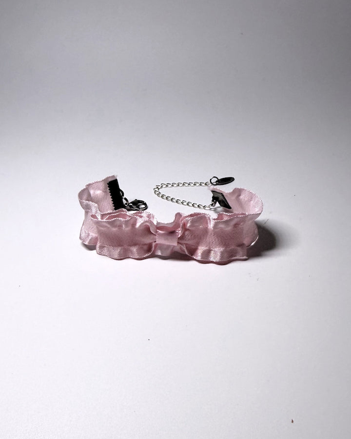 A light pink ruffled bow bracelet and a silver metal chain extender, photographed on a neutral gray background.