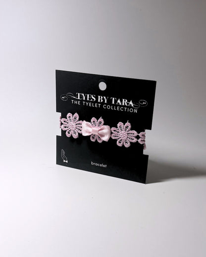 Pink Flower Bow Bracelet displayed on an black retail card on softly lit background