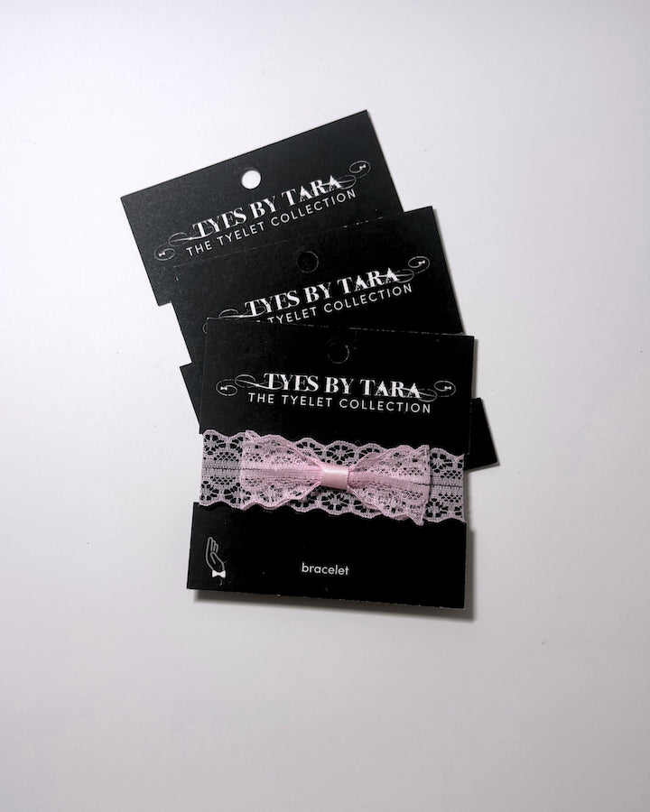 Three black display cards stacked on a white background, each holding a light pink lace bracelet with a matching pink ribbon bow. The cards are branded 'TYLES BY TARA THE TYLET COLLECTION' and label the item as a 'bracelet'.
