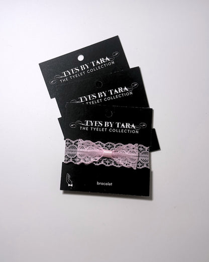 Three black display cards stacked on a white background, each holding a light pink lace bracelet with a matching pink ribbon bow. The cards are branded 'TYLES BY TARA THE TYLET COLLECTION' and label the item as a 'bracelet'.