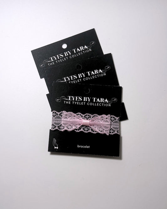 Three black display cards stacked on a white background, each holding a light pink lace bracelet with a matching pink ribbon bow. The cards are branded 'TYLES BY TARA THE TYLET COLLECTION' and label the item as a 'bracelet'.