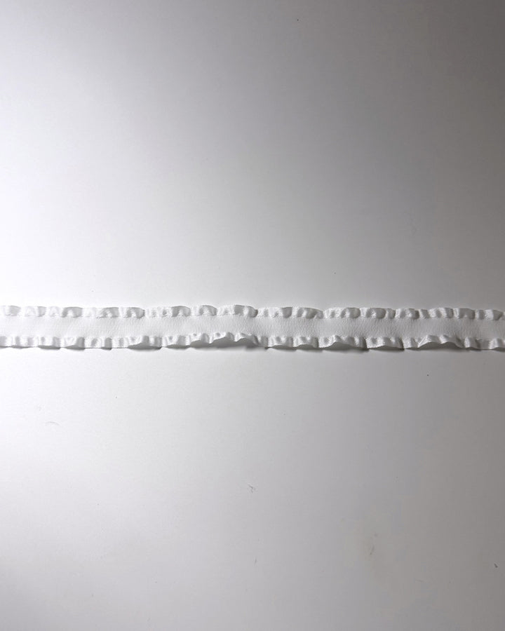A detailed view of the white ruffled trim horizontally across a plain light gray background.