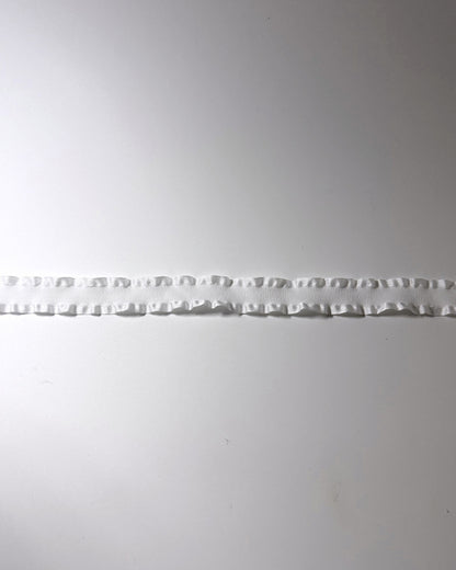 A detailed view of the white ruffled trim horizontally across a plain light gray background.