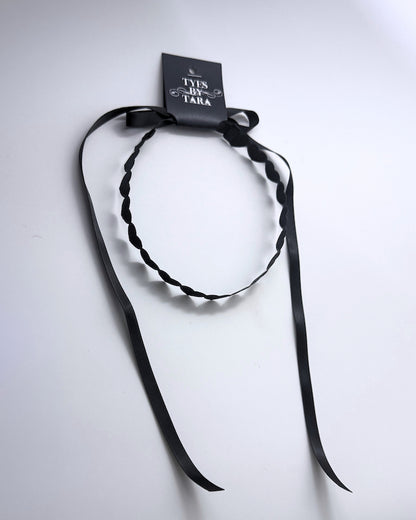 A black heart headband with long ribbon tails, attached to a black paper tag that reads 'TYES BY TARA', photographed on a plain white background.