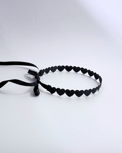 A black heart headband featuring a continuous row of small heart-shaped cutouts and a matching black ribbon tie, displayed on a clean white background.