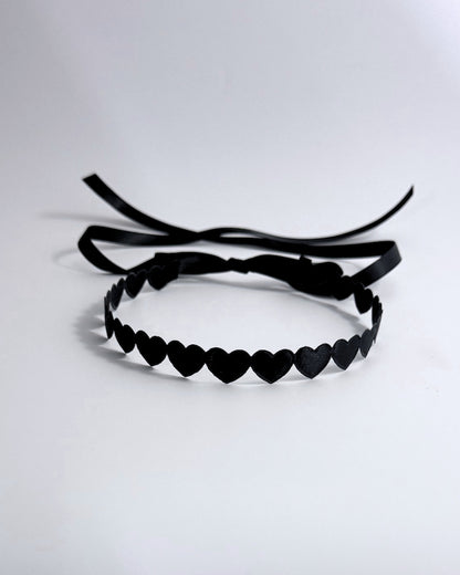 A black headband featuring a continuous row of small heart-shaped cutouts and long ribbon ties, displayed on a clean white background.