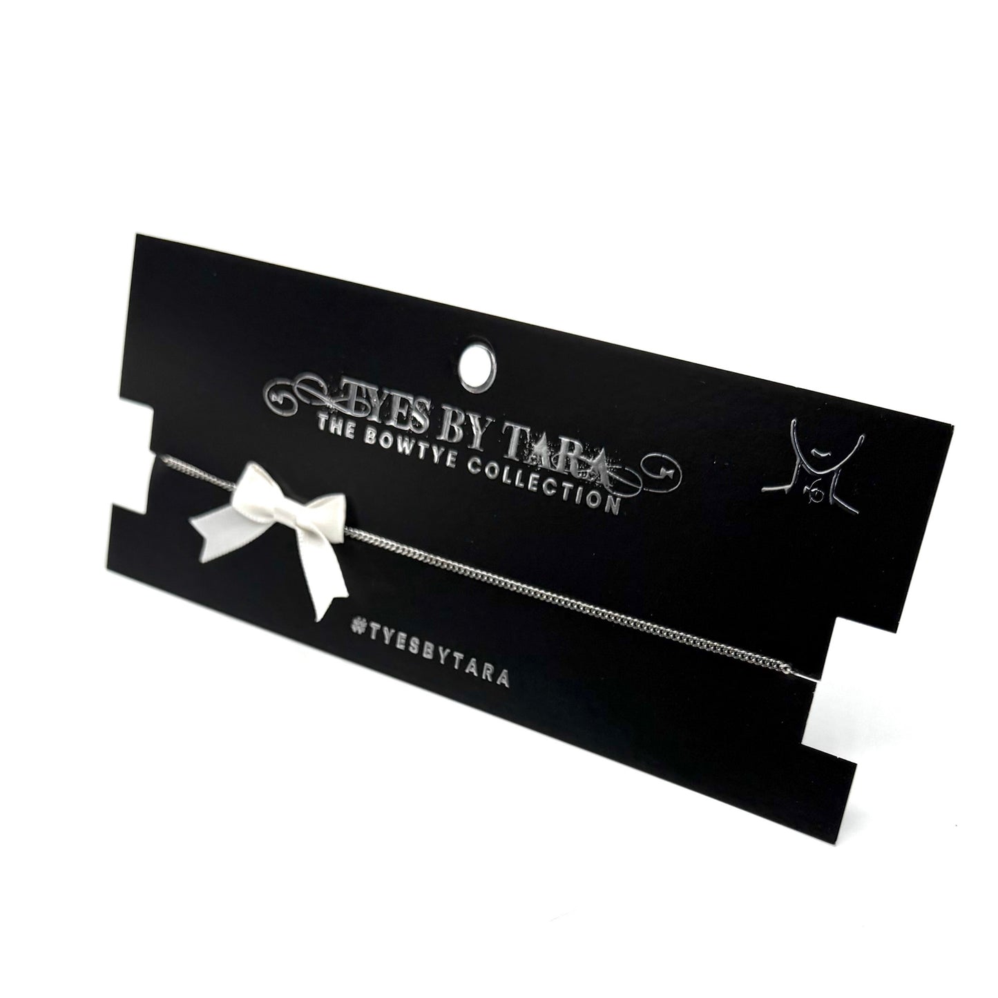 Black card with a white bow necklace jewelry on a white background, featuring 'Tyes by Tara' branding.