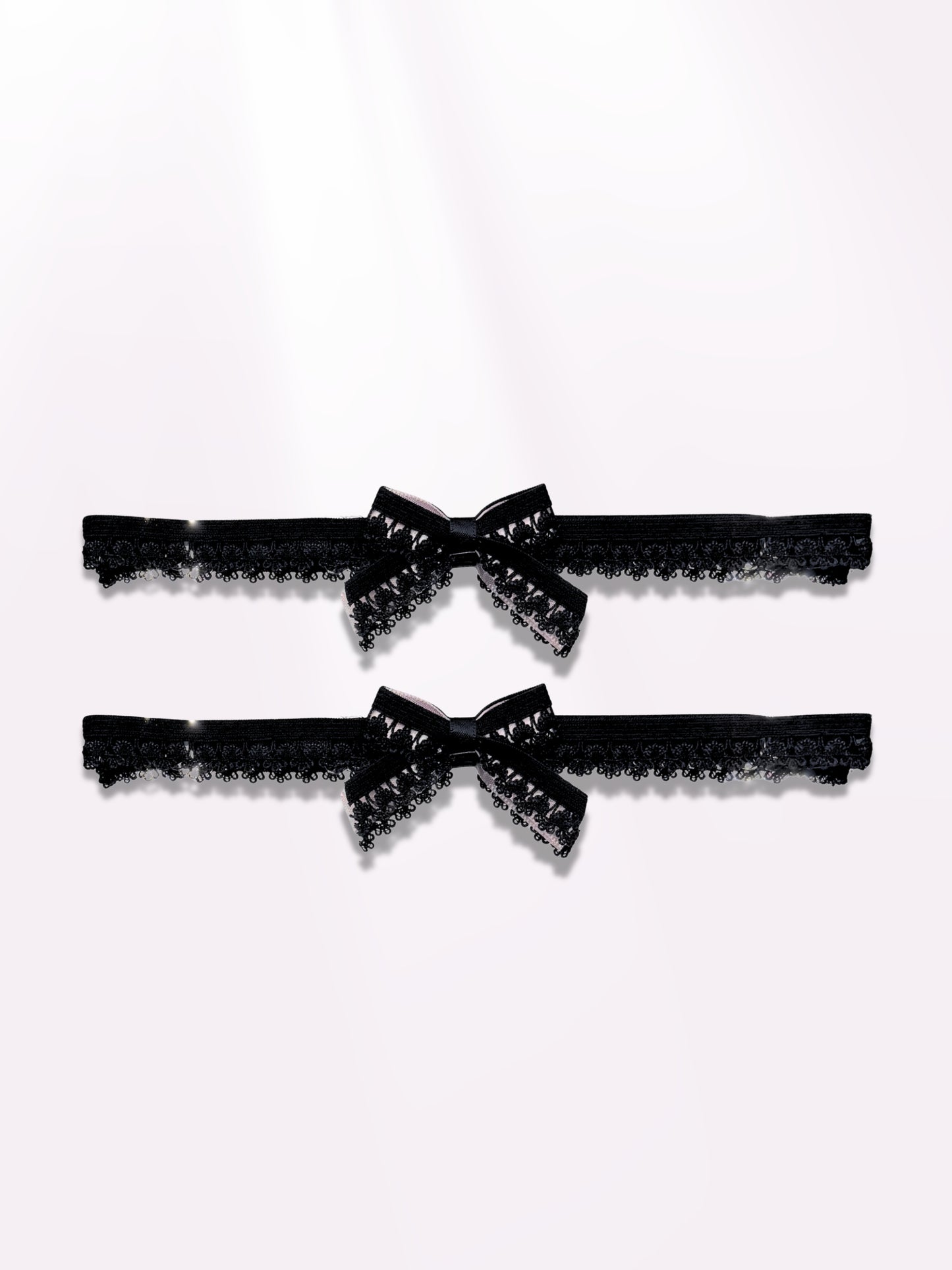 Two black lace elastic garters with bows on light pink background