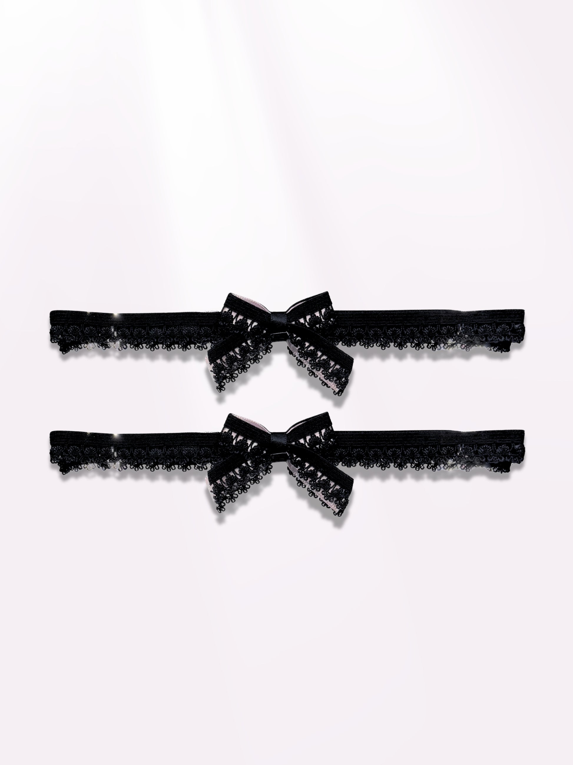 Two black lace elastic garters with bows on light pink background
