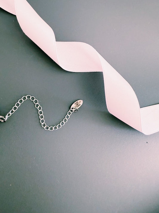 Silver chain with logo tag on a dark surface with a pink ribbon