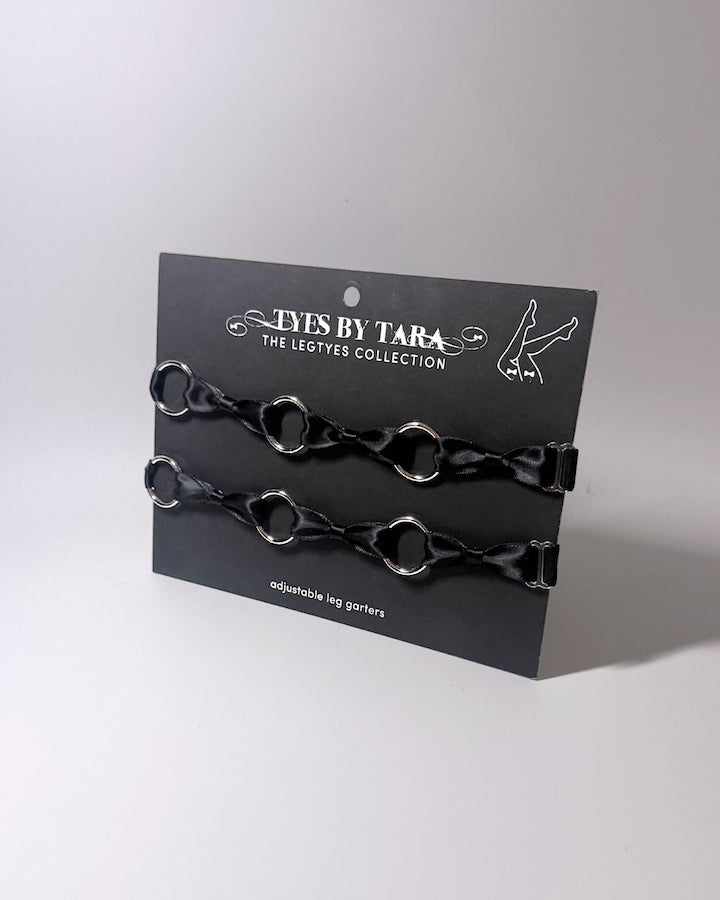 runaway black bow silver o ring leg garters displayed on a black card on softly lit surface